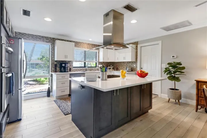 Kitchen with island exhaust hood, white cabinets, light countertops, backsplash, and ornamental molding