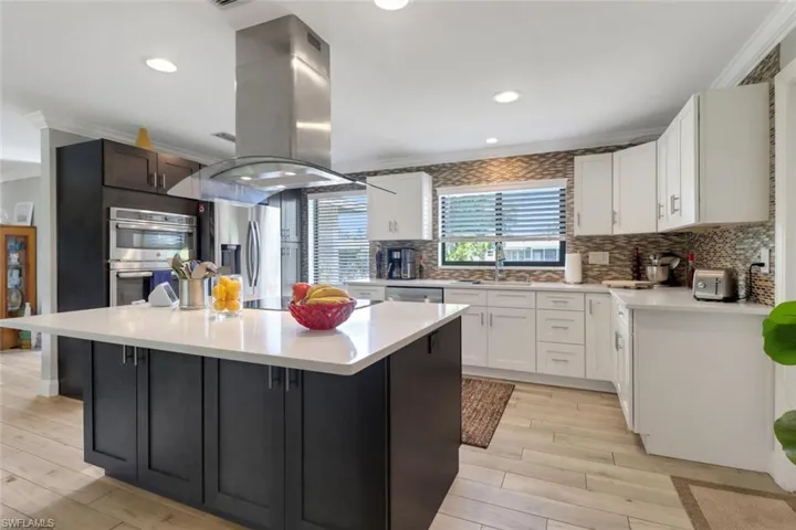 Kitchen featuring island exhaust hood, appliances with stainless steel finishes, crown molding, light countertops, and a center island
