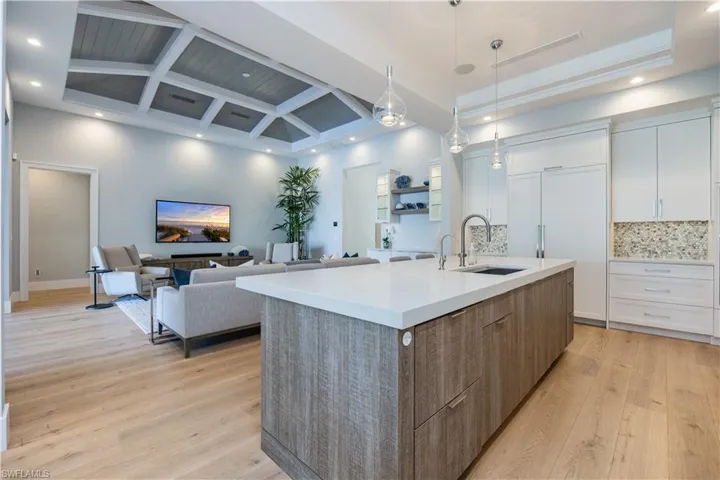 Kitchen featuring white cabinetry, sink, decorative backsplash, a kitchen island with sink, and light wood-type flooring