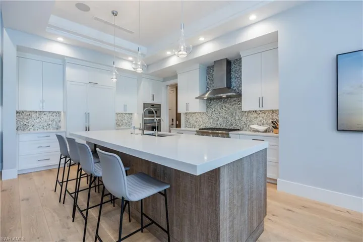 Kitchen with wall chimney exhaust hood, white cabinetry, light hardwood / wood-style flooring, a large island with sink, and a raised ceiling