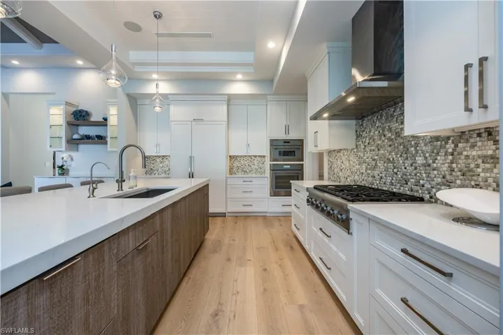 Kitchen with sink, decorative light fixtures, wall chimney range hood, stainless steel gas stovetop, and white cabinets