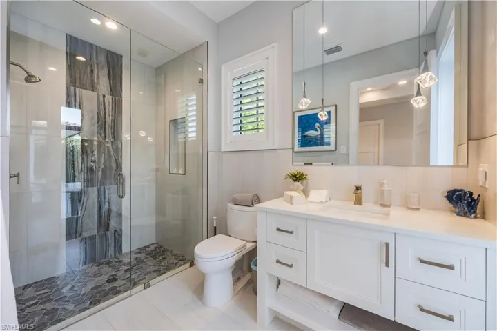 Bathroom featuring tile walls, vanity, a shower with shower door, tile patterned floors, and toilet