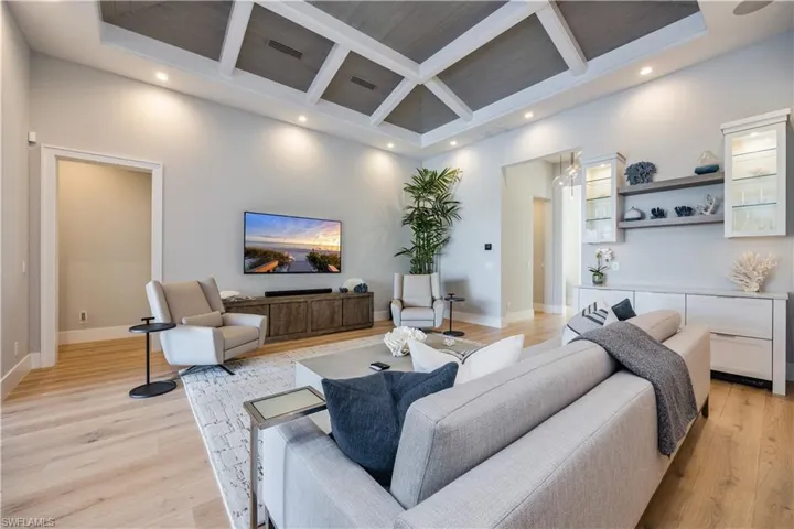 Living room featuring coffered ceiling, beam ceiling, light hardwood / wood-style floors, and a high ceiling
