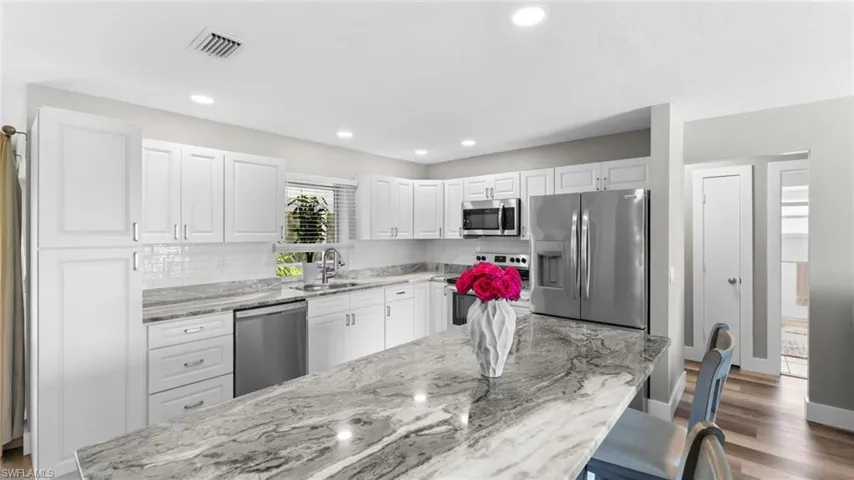 Kitchen featuring light wood-type flooring, decorative backsplash, white cabinets, appliances with stainless steel finishes, and light stone counters
