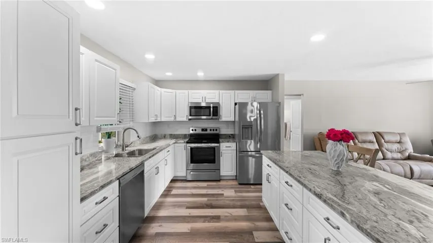 Kitchen with sink, appliances with stainless steel finishes, hardwood / wood-style flooring, decorative backsplash, and white cabinets
