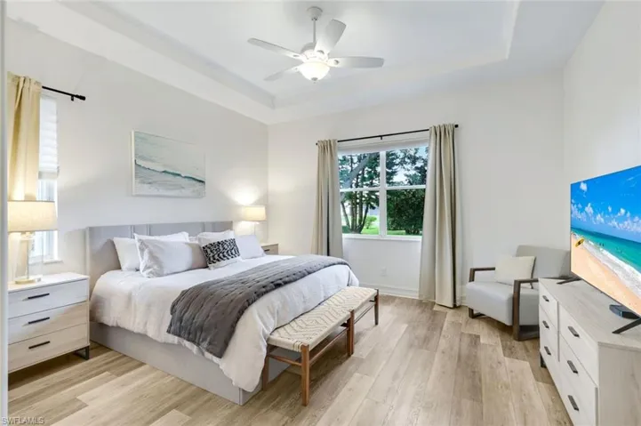 Bedroom featuring a tray ceiling, light wood plank LVT finished floors, and ceiling fan