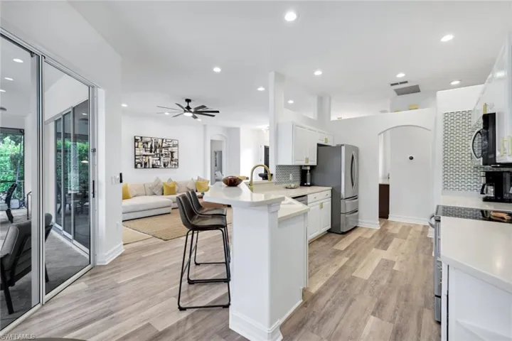 Kitchen with arched walkways, a peninsula, white cabinetry, backsplash, and recessed lighting