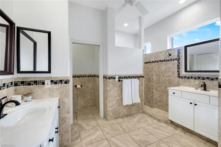 Full bathroom featuring tile walls, two vanities, walk in shower, and ceiling fan