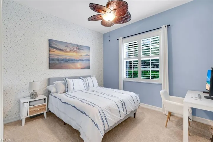 Bedroom featuring light colored carpet, ceiling fan, wallpapered walls, and a desk