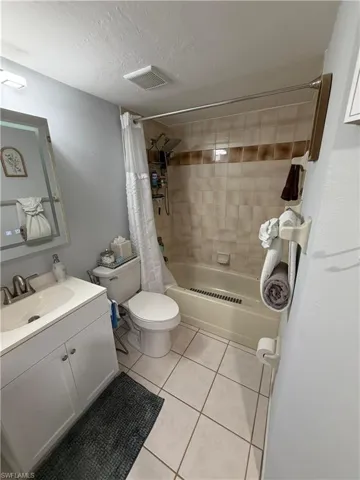 Bathroom featuring a tile-surround bathtub, white vanity with integrated sink, brushed nickel faucet, and square tile flooring