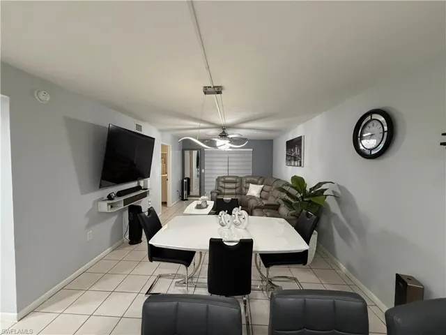 Open-concept living area featuring light-toned tile flooring, a wall-mounted media console, and a contemporary ceiling fan with integrated lighting