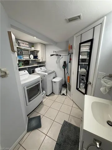 Utility room featuring a built-in vanity with an integrated sink, tiled flooring, and a dedicated laundry area with overhead cabinetry and shelving