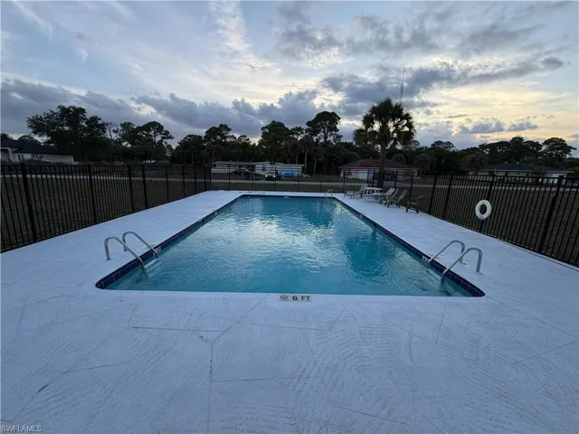 Rectangular swimming pool with white textured decking and a black metal fence