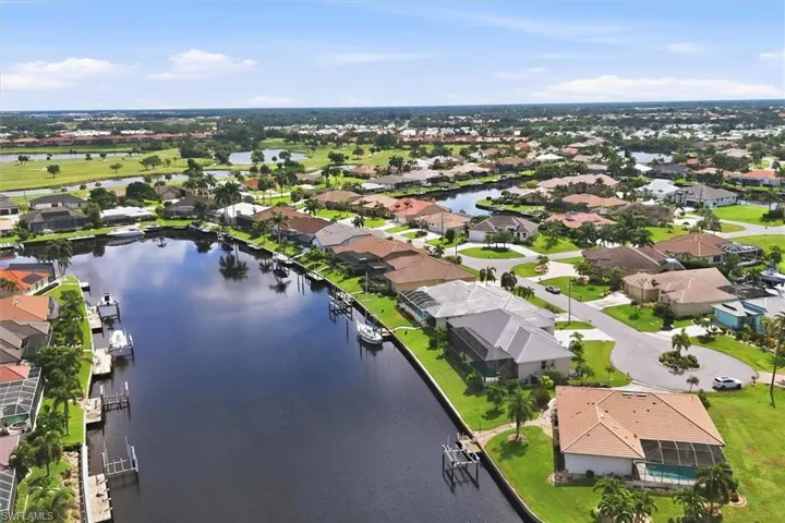 Waterfront property with private boat docks, surrounded by manicured lawns and mature trees, featuring a screened pool enclosure