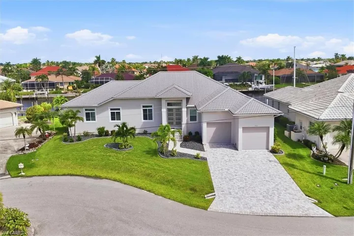 Modern exterior with a tiled roof, paver driveway, two-car garage, and a manicured lawn with tropical landscaping