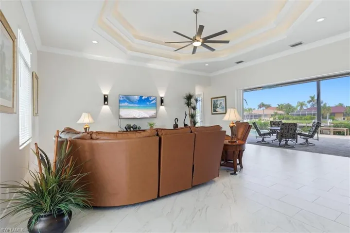 Tray ceiling with crown molding, ceiling fan, white large-format tile flooring, and a screened patio with outdoor dining