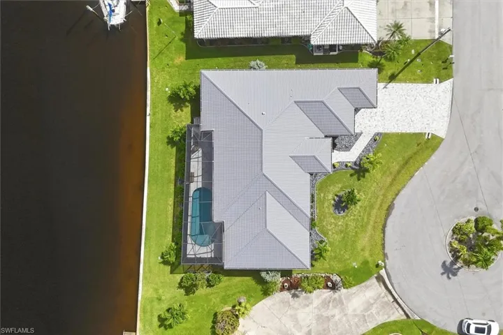 Waterfront property featuring a screened pool enclosure, a paved driveway, a gray tile roof, and landscaped grounds