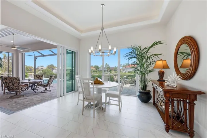 White tile flooring, tray ceiling, sliding glass doors, screened patio, and a chandelier