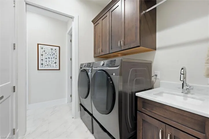 Laundry room featuring wood-finish cabinetry, a built-in sink with a polished chrome faucet, a white countertop, and light-toned tile flooring