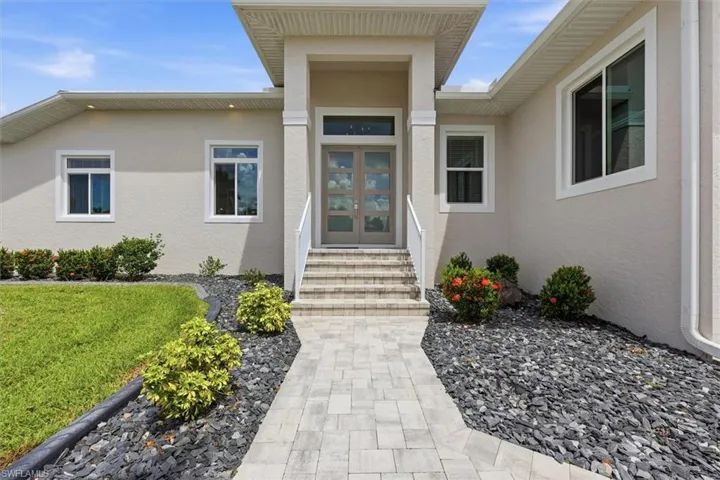 Contemporary stucco exterior with a covered entry, double glass-paneled entry doors, and paver walkway