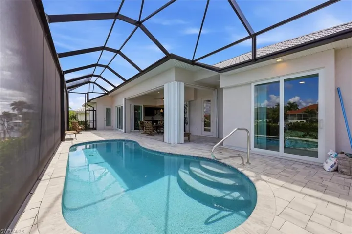 Screened outdoor living area with a built-in swimming pool, paved pool deck, and retractable glass doors