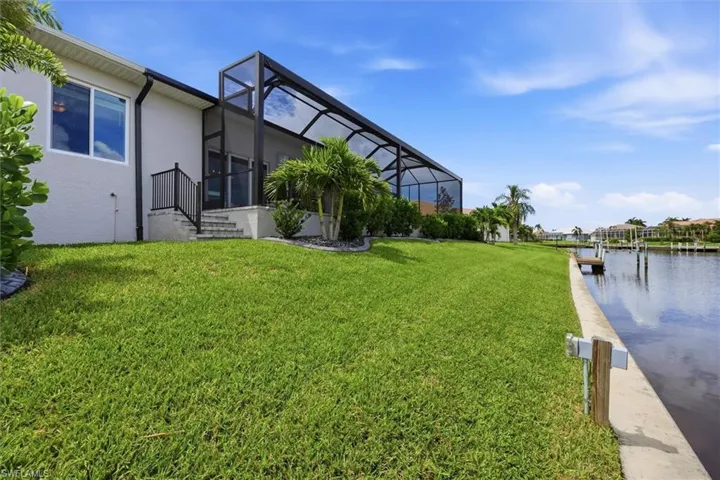 Screened-in patio with sliding glass doors, leading to a landscaped yard with mature palms and a concrete seawall