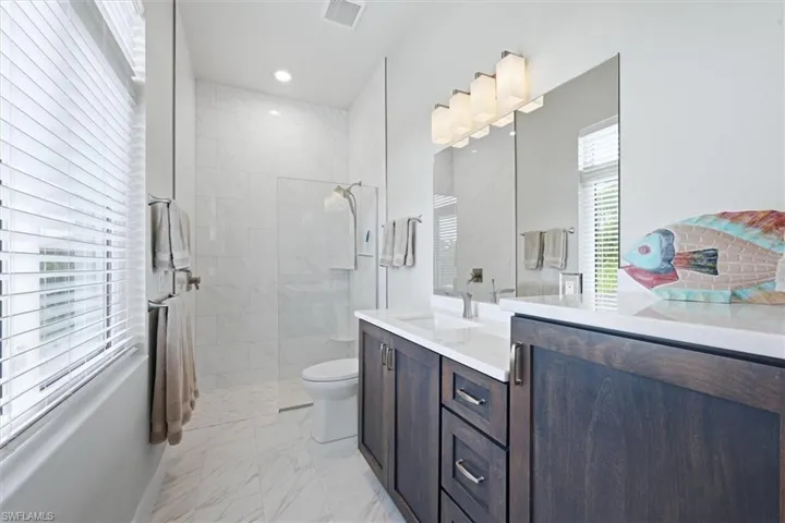 Spacious bathroom featuring a dual vanity with dark wood-finish cabinetry, light countertops, a walk-in shower with tile surround, and large format floor tiling