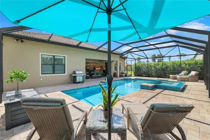 View of pool featuring a lanai, an outdoor eating area,a grill, TV, pool with waterfall