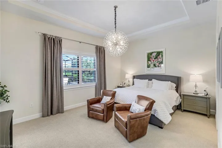 Ensuite bedroom featuring ornamental molding, a tray ceiling, and a decorative designer chandelier