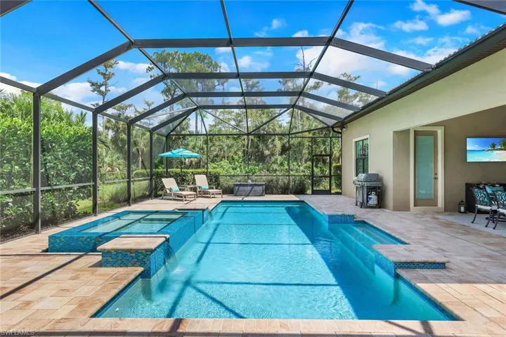 View of swimming pool featuring very large screened lanai and hot tub with waterfall