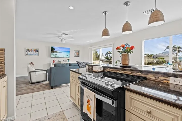 Kitchen featuring cream cabinetry, black range with electric cooktop, pendant lighting, dark stone counters, and light tile patterned flooring