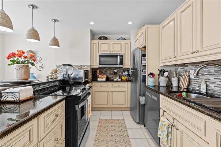 Kitchen with cream cabinets, dark stone counters, decorative light fixtures, appliances with stainless steel finishes, and recessed lighting