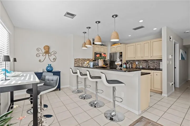 Kitchen with cream cabinetry, a breakfast bar area, a peninsula, freestanding refrigerator, and pendant lighting