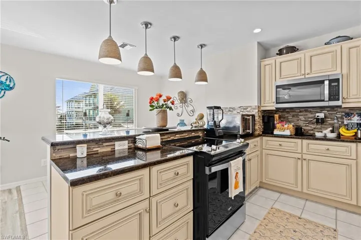 Kitchen with cream cabinetry, black electric range oven, decorative backsplash, hanging light fixtures, and dark stone counters