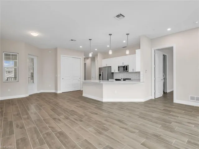 Kitchen with open floor plan, decorative light fixtures, stainless steel appliances, white cabinets, and wood finish floors