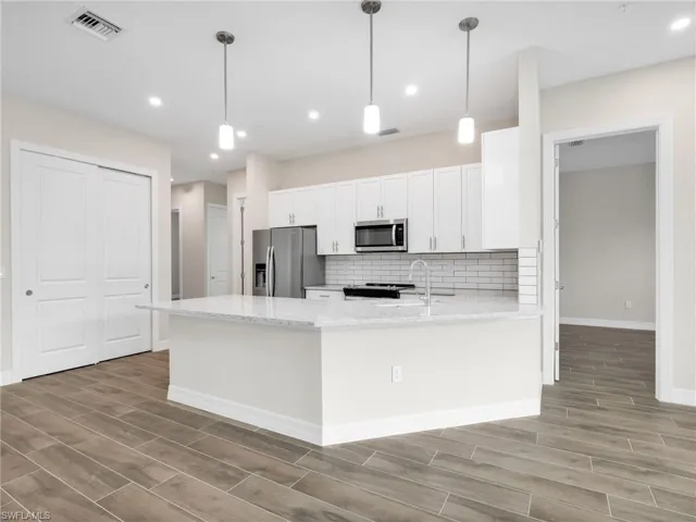 Kitchen featuring pendant lighting, wood tiled floors, light stone counters, a peninsula, and stainless steel appliances