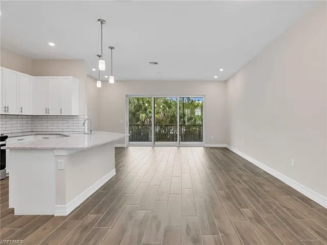 Kitchen featuring hanging light fixtures, white cabinetry, wood finish floors, decorative backsplash, and light stone countertops