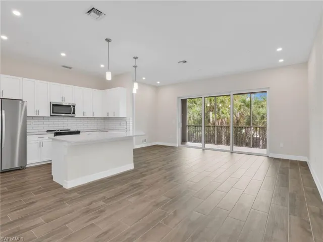 Kitchen with stainless steel appliances, decorative light fixtures, open floor plan, white cabinetry, and wood finish floors