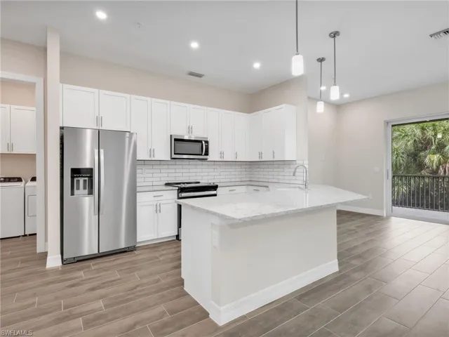 Kitchen featuring stainless steel appliances, wood finish floors, hanging light fixtures, a peninsula, and light stone counters