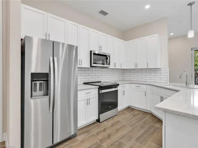 Kitchen with stainless steel appliances, light stone counters, white cabinetry, decorative light fixtures, and wood finish floors