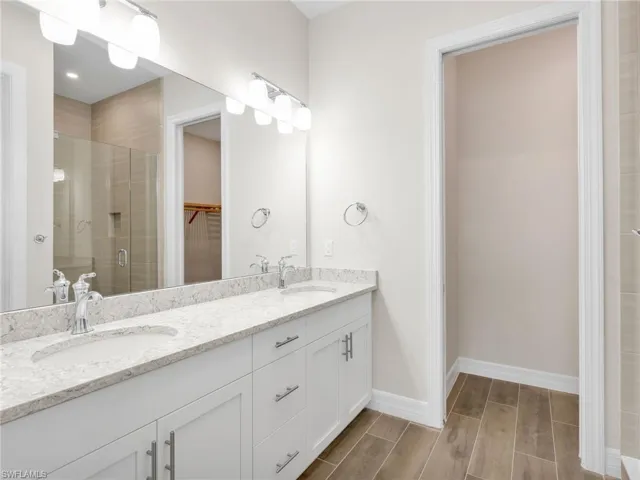 Full bath with a stall shower, double vanity, wood tiled floors, and a walk in closet