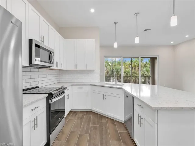 Kitchen featuring stainless steel appliances, hanging light fixtures, a peninsula, and light stone counters