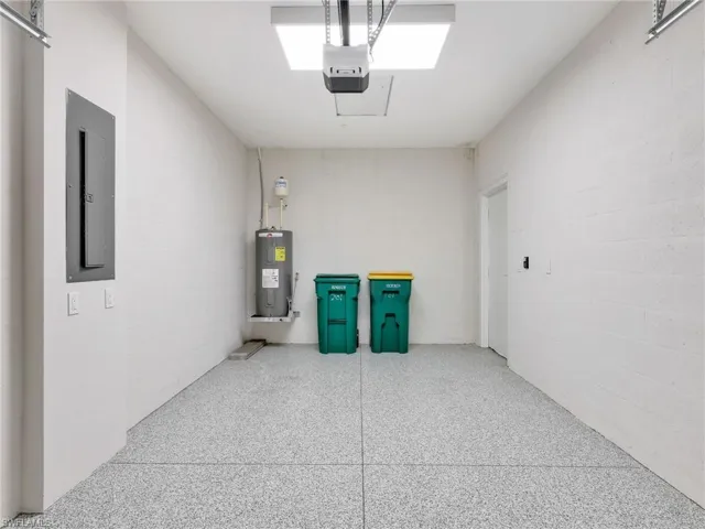 Garage featuring concrete block wall, electric panel, water heater, and a garage door opener