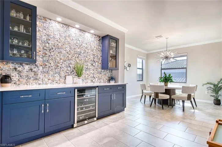 Indoor bar with glass insert cabinets, crown molding, wine cooler, blue cabinets, and light tile patterned floors
