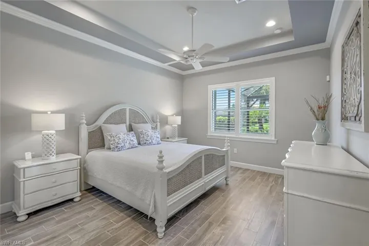 Bedroom with wood finish floors, ornamental molding, a raised ceiling, recessed lighting, and ceiling fan