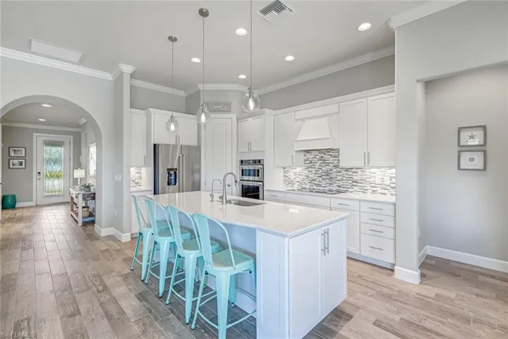Kitchen with arched walkways, recessed lighting, appliances with stainless steel finishes, ornamental molding, and custom exhaust hood