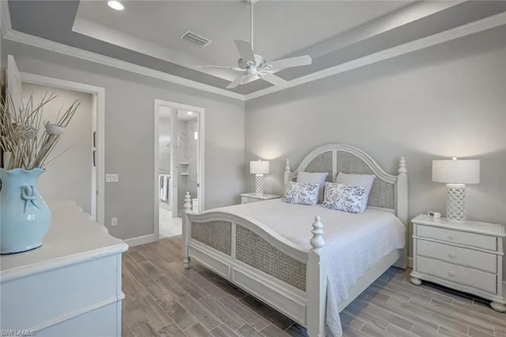 Bedroom with ornamental molding, a tray ceiling, wood tiled floors, connected bathroom, and recessed lighting