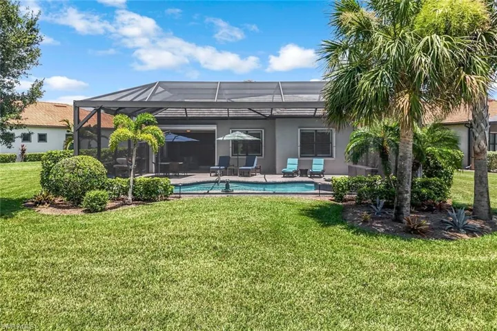 Rear view of house with stucco siding, a lawn, an outdoor pool, a patio area, and glass enclosure
