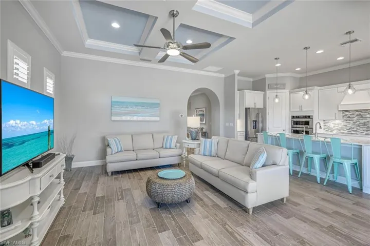 Living room with arched walkways, light wood-type flooring, recessed lighting, coffered ceiling, and ornamental molding