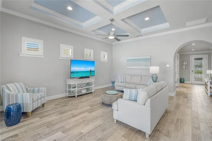 Living room with arched walkways, coffered ceiling, recessed lighting, crown molding, and beam ceiling